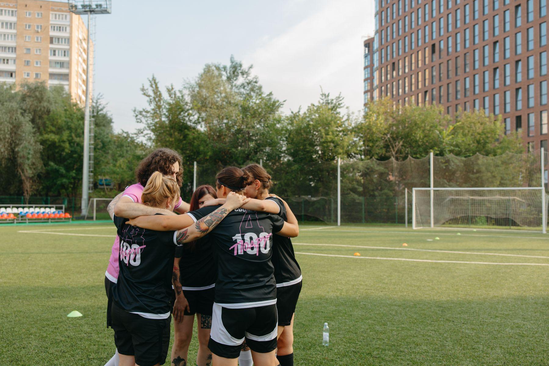 A women's football team gathered in a huddle on an outdoor pitch